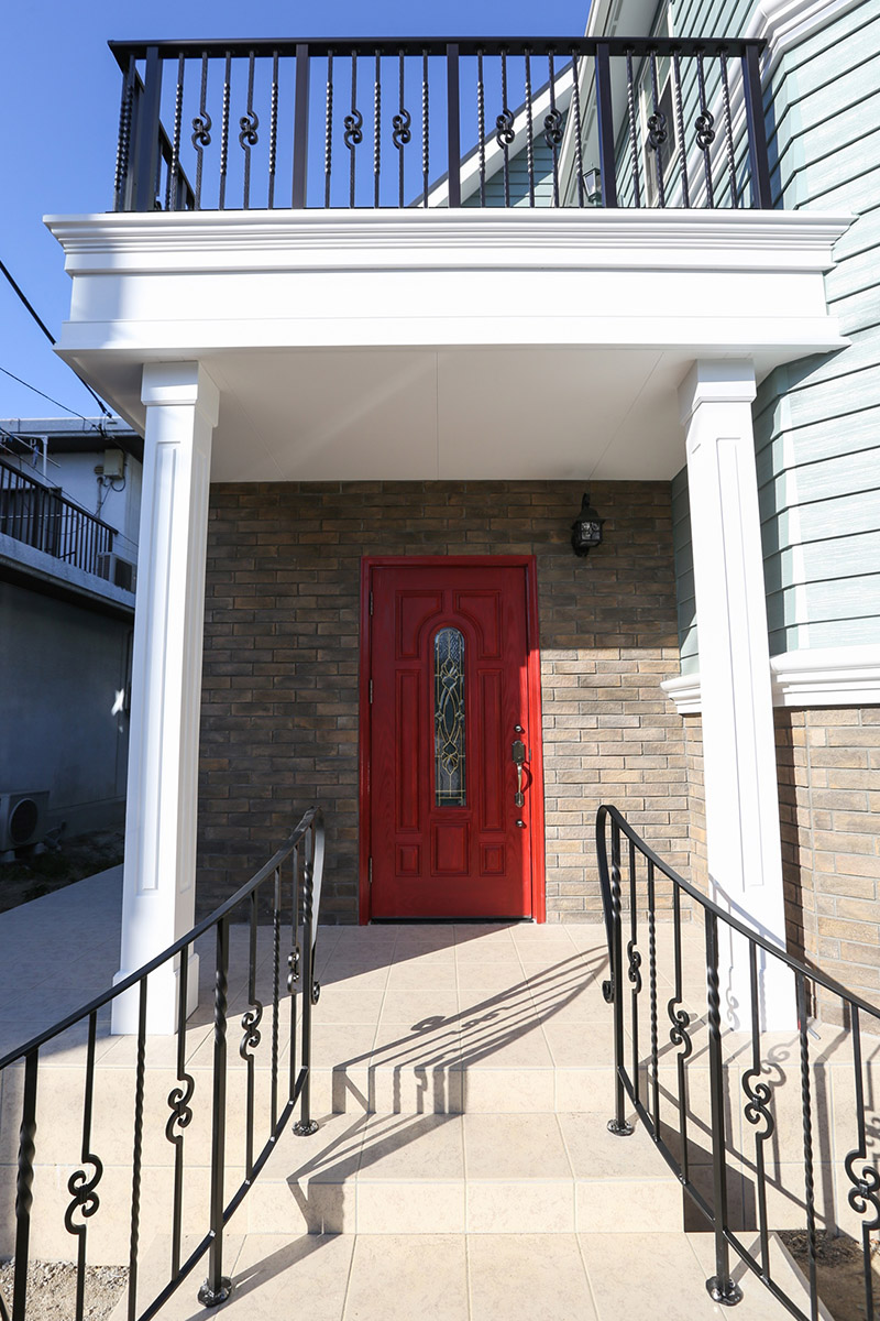 玄関：サイディングのブルーグレー、 輸入ドアの赤、レンガのブラウン、アイアンのブラックに飾柱の白。多素材多色を合わせシックに。