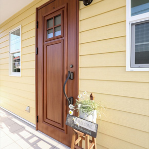 玄関：ウォームイエローのサイディングにほっこり色の木製ドアが、訪れる人をあたたかく迎えます。