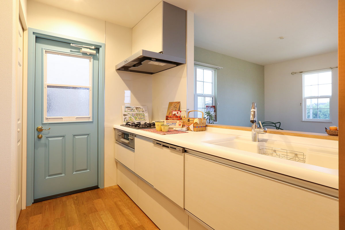 キッチン：インテリアを邪魔しないミルクホワイトのキッチンには、ブルーグレーのドアが優しいアクセントに。