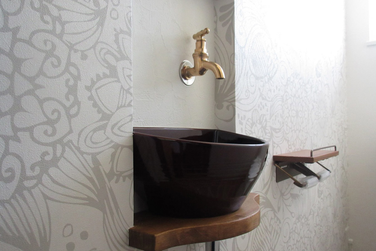 洗面：トイレ内に設けられたニッチ＋ミニ手洗い。シックな柄クロスと陶器ボウルのブラウンがマッチ。