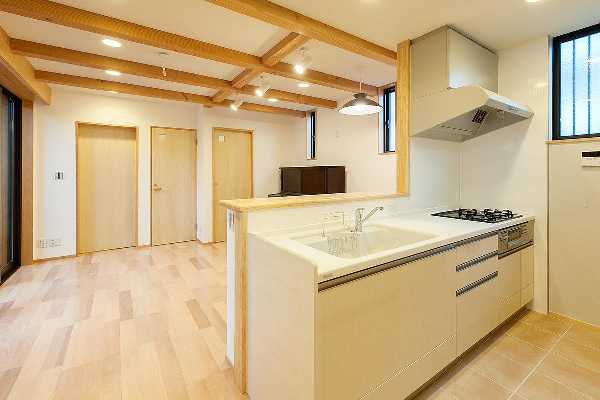 １階親世代のリビングダイニングキッチンは、天井に構造体の無垢の梁を見せるデザイン。キッチンはタイル貼りでお掃除も簡単。
