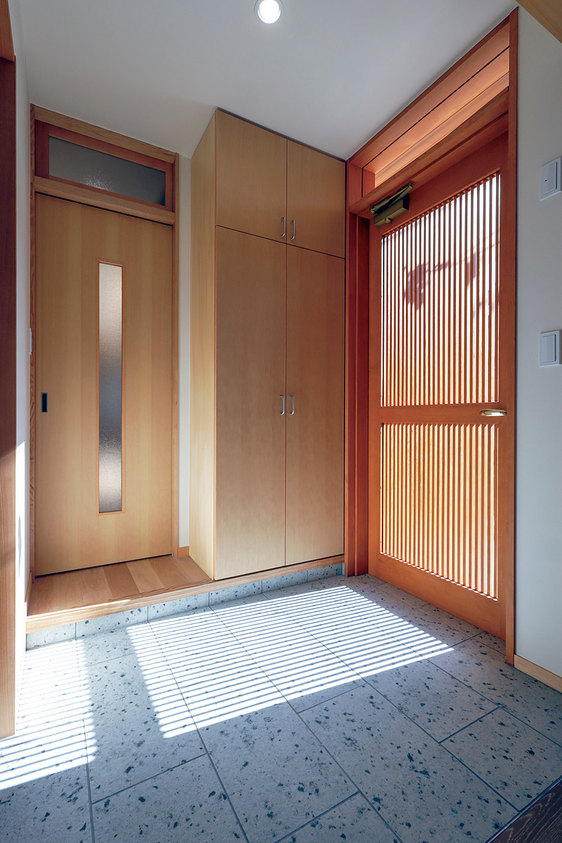 玄関床は大谷石調のタイル貼り、玄関扉は細かい縦桟の木製扉にしています。
