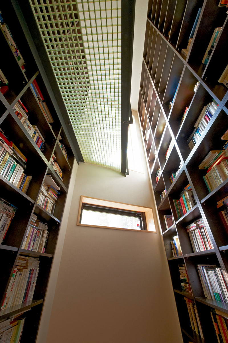 地下から1階を見上げる書棚、棚板を少し傾け落ちにくい