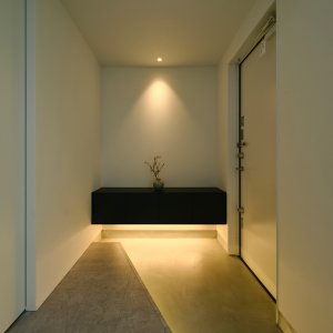 シンプルで落ち着いた玄関ホール。黒い浮遊棚と間接照明が印象的。ミニマルな美しさが際立つ空間