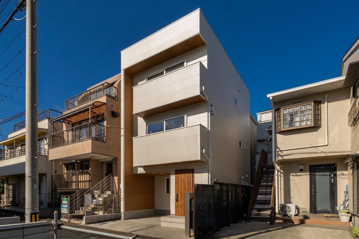 青空に映える3階建ての外観、木目調アクセントが印象的な都市型住宅