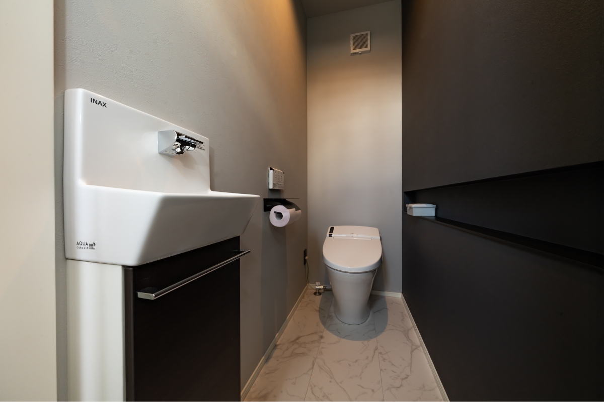 壁掛け手洗い器とダークカラー壁面を組み合わせた、上質な陰影のトイレ空間