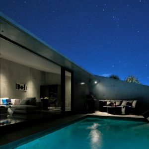 星空の下のプール。壁に囲まれた中庭のような屋外空間と、灯りの入ったリビング 星空の下のプール。壁に囲まれた中庭のような屋外空間と、灯りの入ったリビング
