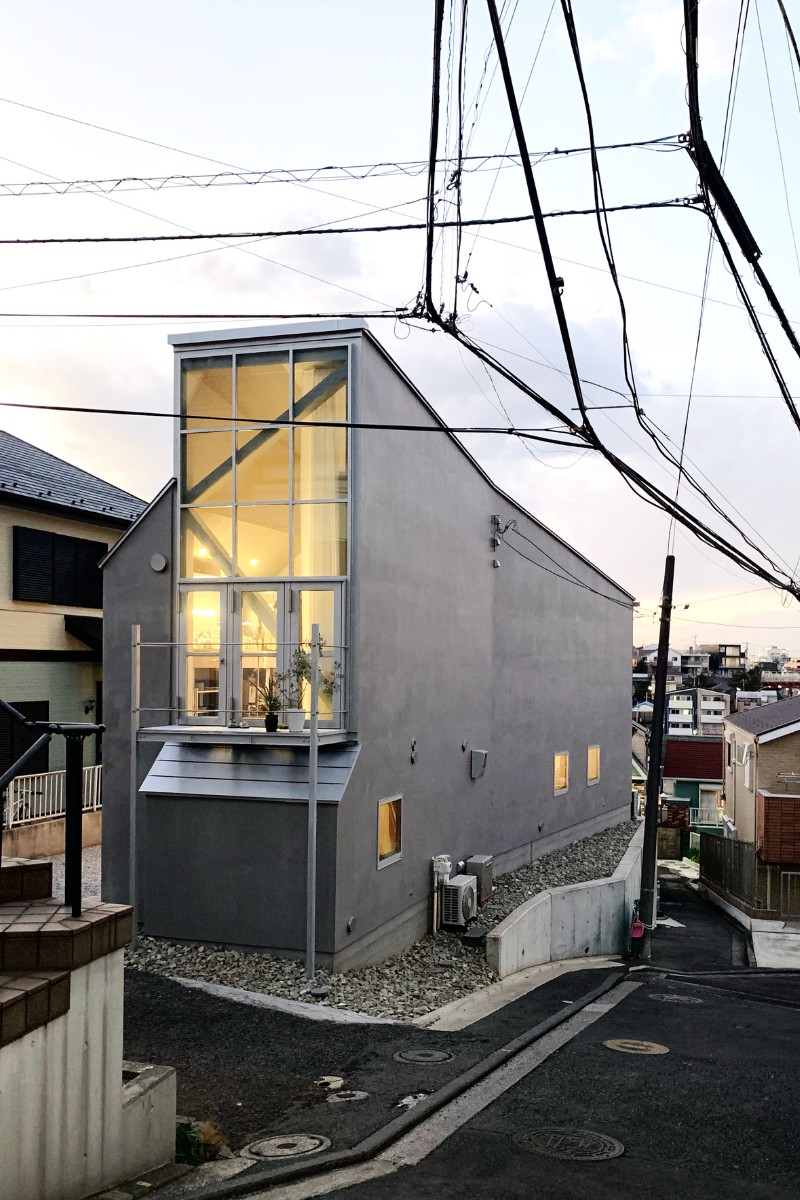 道路に面した2層分の大開口が特徴の丘陵地の崖地に建つ住宅外観