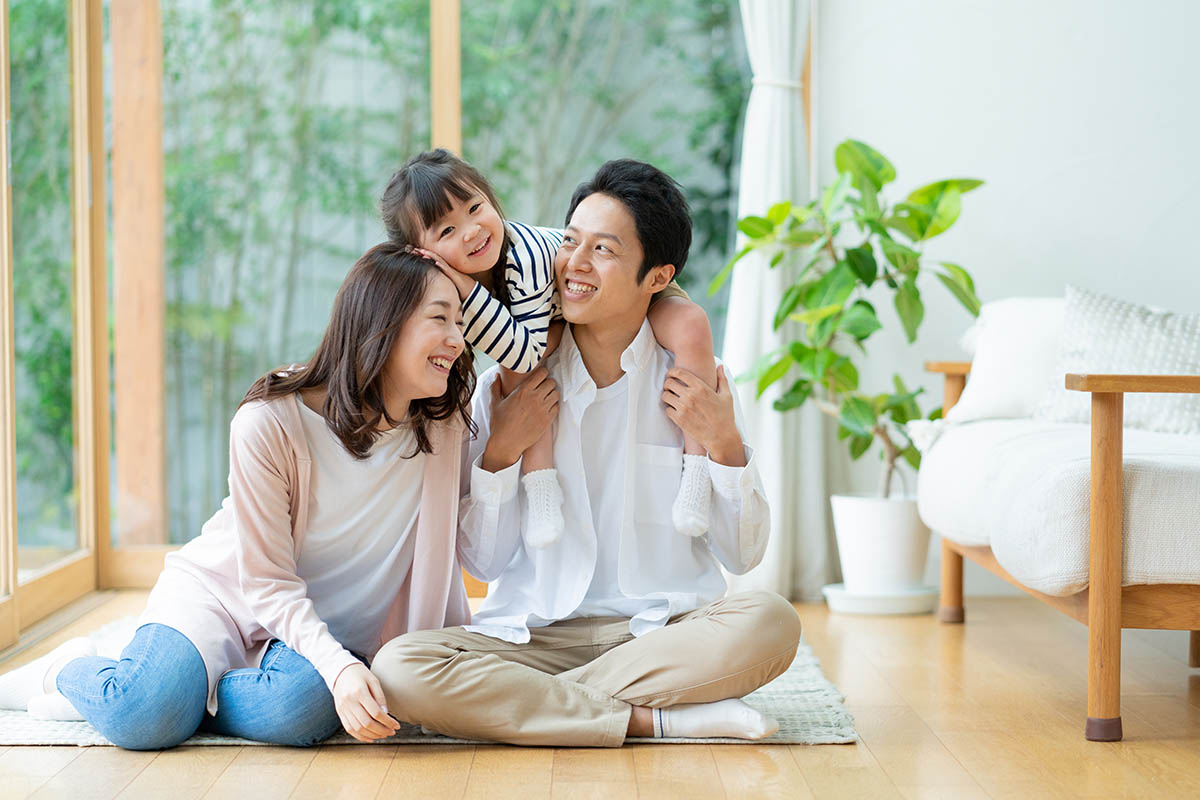 リビングに座ってパパに肩車をされてふざける女の子とパパとママの3人家族のポートレート