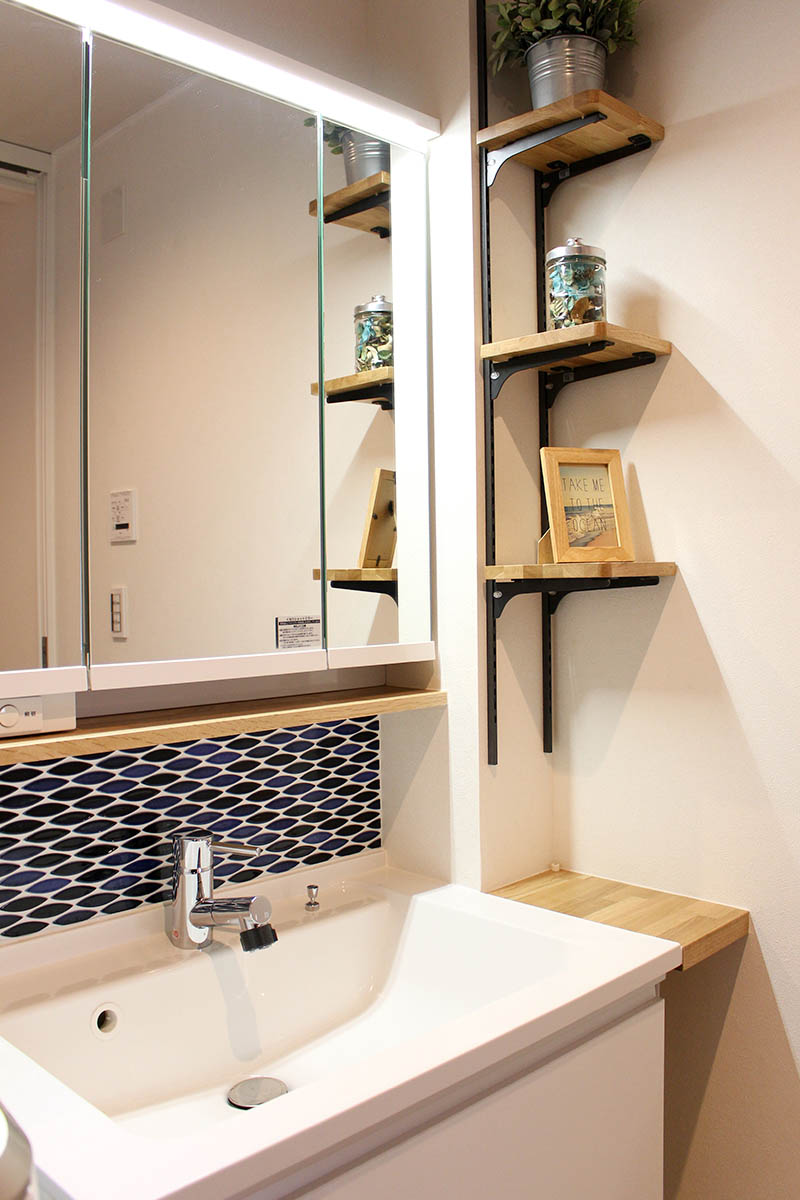 青いモザイクタイルが印象的な洗面台。その横に木の造作棚を設置し、おしゃれにデッドスペースを有効活用。