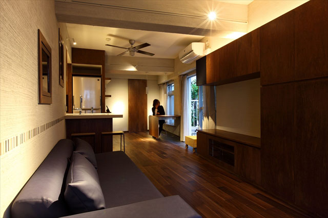 ベランダ側からリビング。オープンキッチン、ソファー、大人っぽい色使いの収納と程よい明るさの照明が落ち着いた空間を演出。