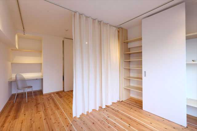 壁面収納に隠されたリネンのカーテンを引くことで、ワンルームの中央で二つの空間に間仕切ることができます。